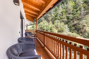 A wooden balcony with two wicker chairs, overlooking a forested hillside.
