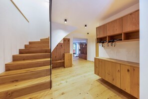 Una escalera de madera que lleva al segundo piso, un armario de madera con ganchos y un pasillo con suelo de madera.