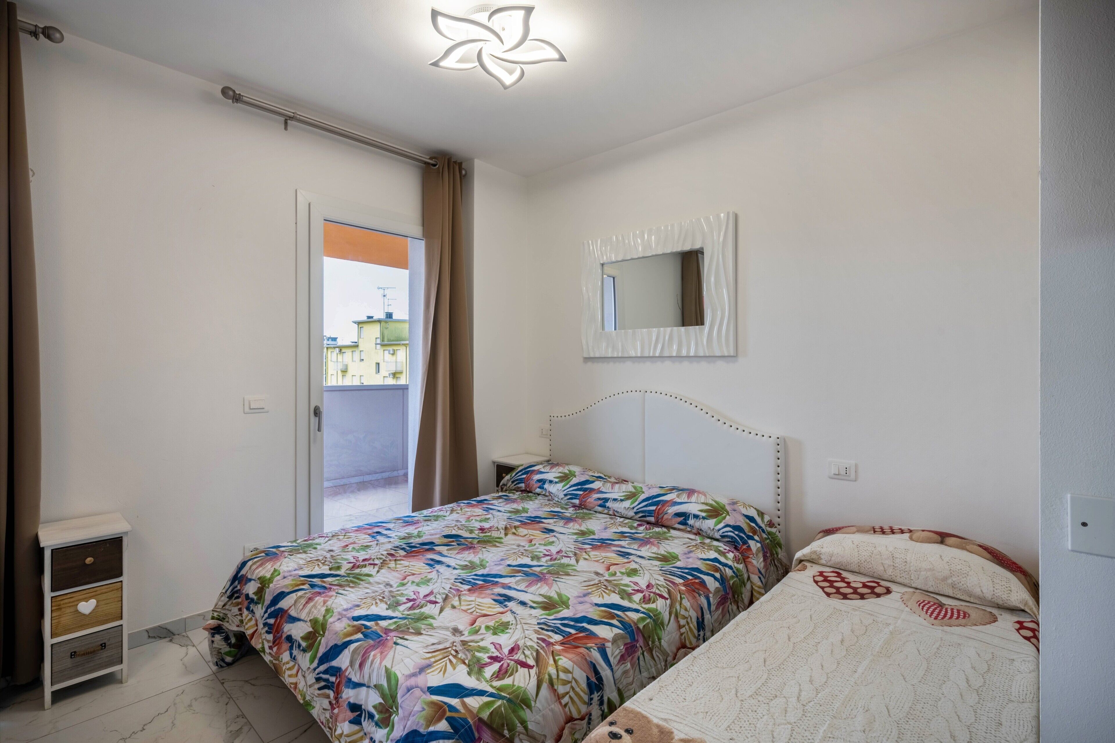 Une chambre à coucher comprenant un lit, une table de chevet, un miroir et une porte donnant sur un espace extérieur.