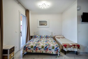 Un dormitorio con una cama, una cama individual, un espejo, un televisor y una puerta.