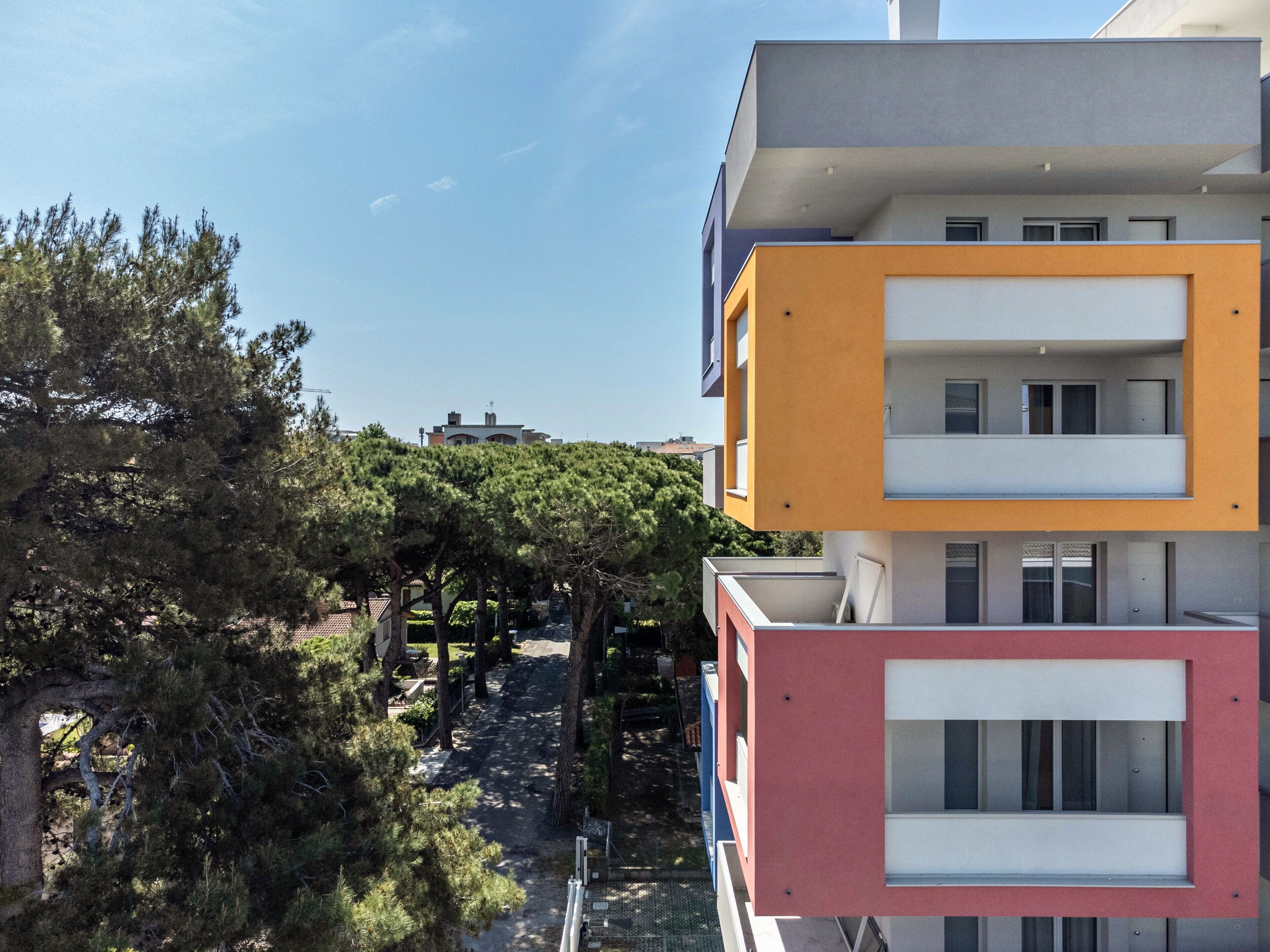 Un immeuble à plusieurs étages doté de balcons, un ciel dégagé et des arbres au premier plan.