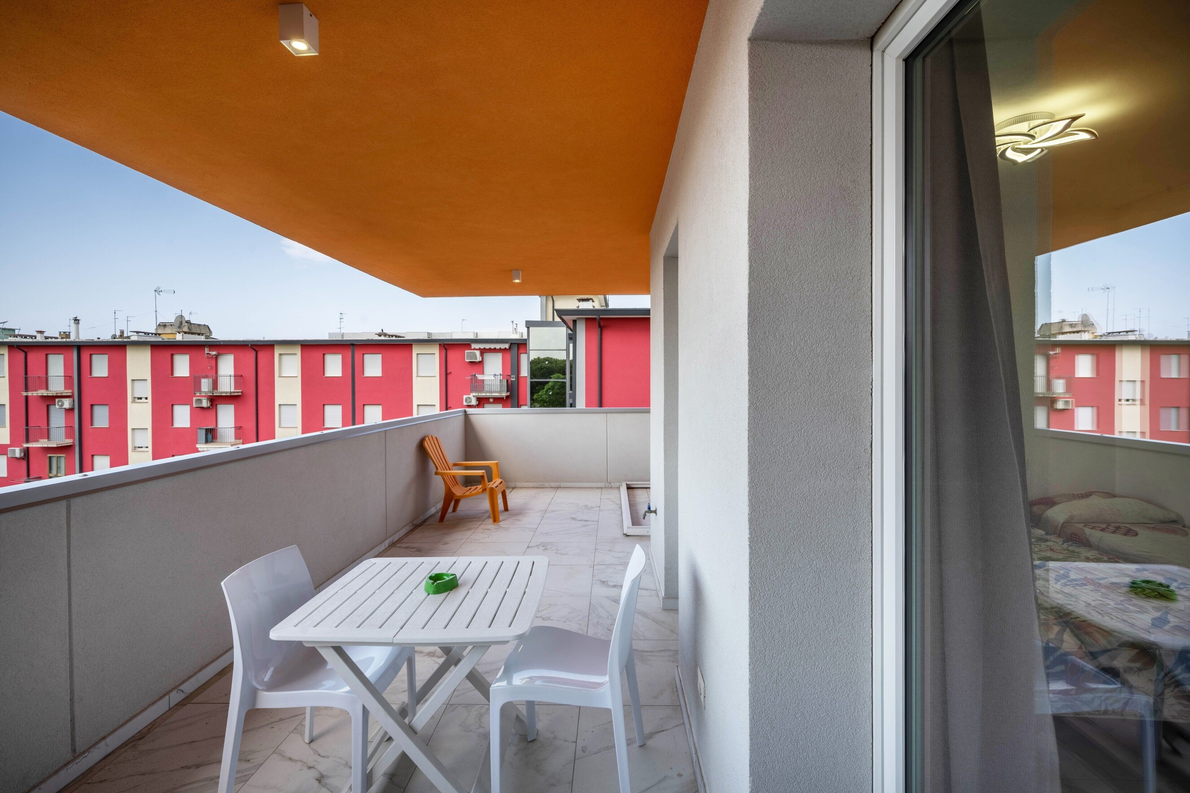 Un balcon avec une table et des chaises, une fenêtre et une vue sur des bâtiments rouges.
