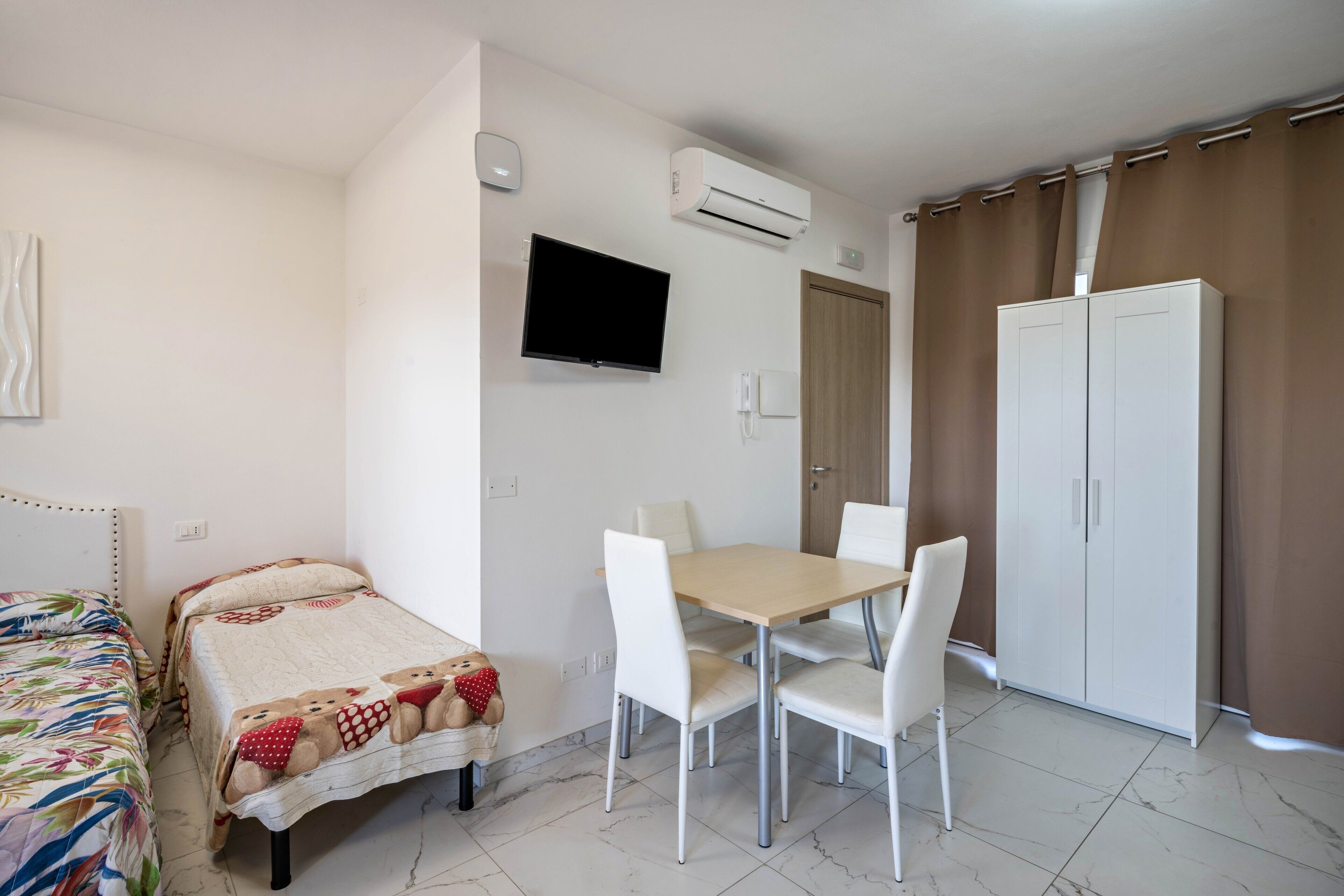 Une chambre à coucher comprenant un lit, une table de chevet, une télévision, un climatiseur, une armoire et une porte menant à la salle de bain.