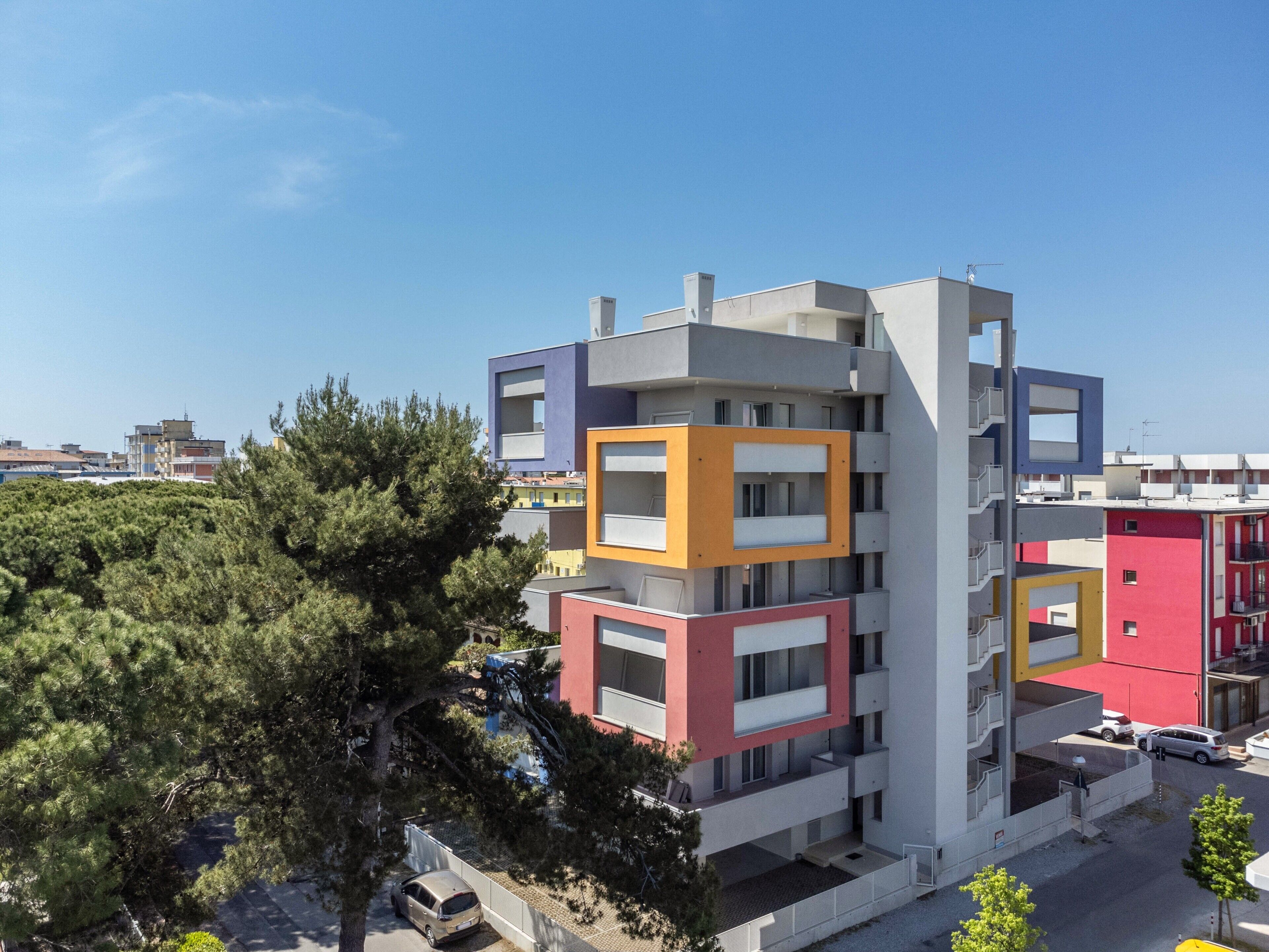Un immeuble résidentiel à plusieurs étages, doté de balcons, d’un espace de stationnement et surplombant un ciel dégagé.