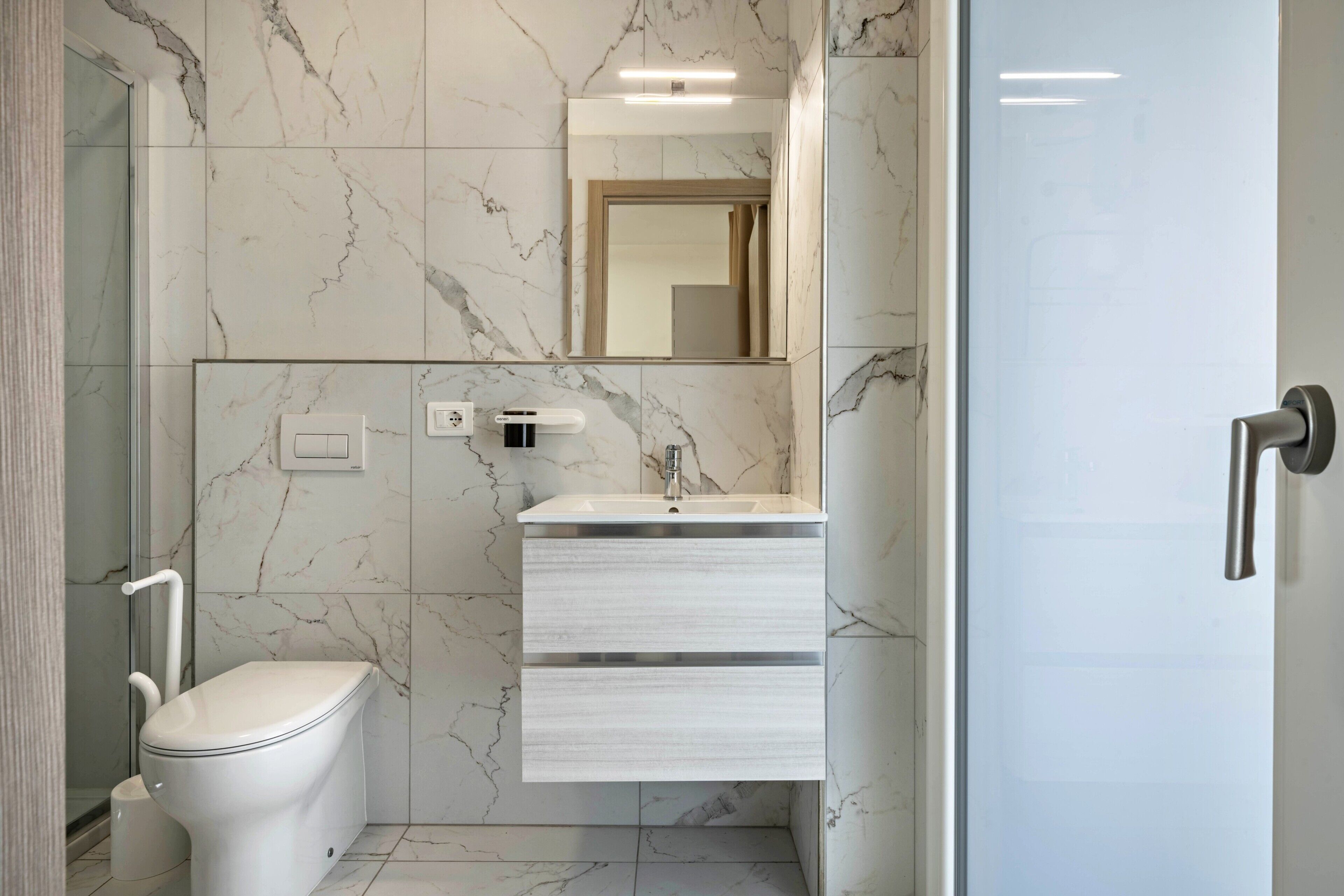 Un baño moderno con inodoro, lavamanos con espejo y cabina de ducha.
