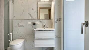 Un baño moderno con inodoro, lavamanos con espejo y cabina de ducha.
