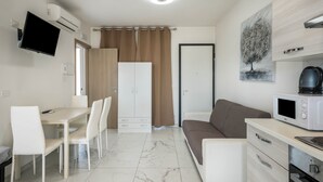 Une pièce moderne et bien éclairée, comprenant une table à manger, des chaises, un canapé, un téléviseur, un four à micro-ondes et un tableau accroché au mur.