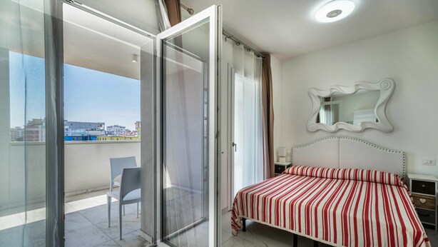 Une chambre à coucher comprenant un lit, une porte-fenêtre coulissante donnant sur un balcon, un miroir au mur et une table de chevet.