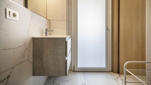 Une salle de bain avec un mur en marbre, un meuble-lavabo en bois, un lavabo blanc et une porte avec un panneau en bois.