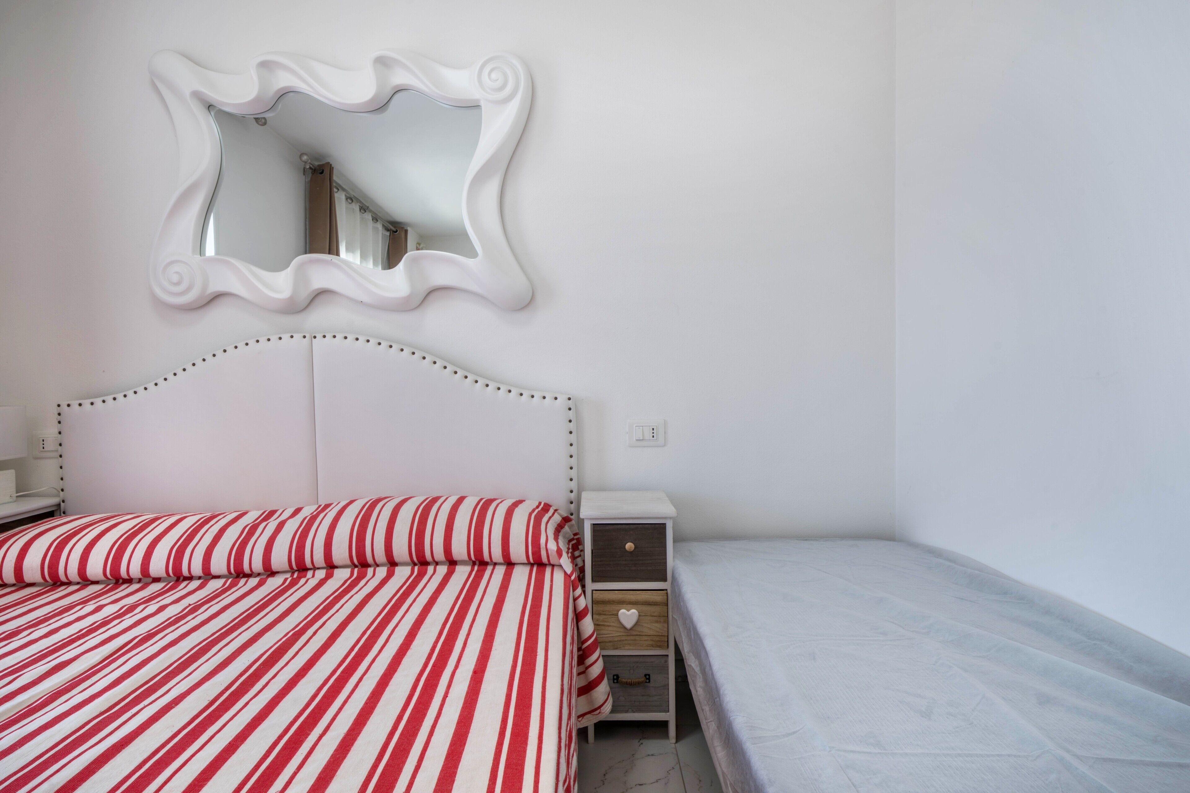 Una camera da letto con un letto a righe, un comodino, uno specchio e un mobiletto.
