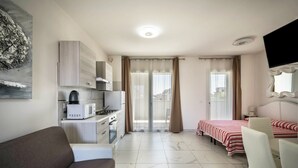 Une chambre d’hôtel compacte comprenant un coin cuisine, un canapé, un lit avec une couvre-lit à rayures et un téléviseur fixé au mur.