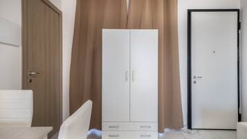 A room with a white wardrobe, a wooden door, a white chair, and a closed door with a handle.