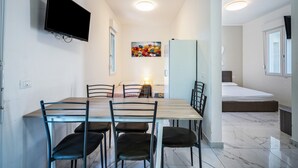 A compact room with a dining table, chairs, a TV mounted on the wall, a bed, and a painting on the wall. - Holiday Apartment "Residenza Maja 6" with Wi-Fi (San Michele al Tagliamento)