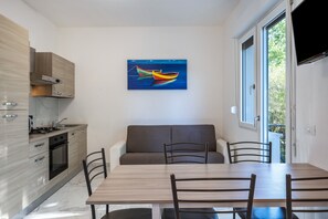 A modern kitchen with wooden cabinets, a dining table with chairs, and a painting of a boat on the wall.