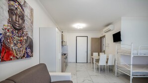 A modern room with a sofa, bunk beds, a dining table, chairs, a kitchen area, and a TV. - Studio Apartment "Planet Suite 303 Bibione" with Wi-Fi (San Michele al Tagliamento)