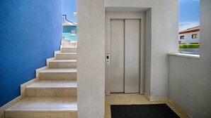 A staircase leading to an elevator in a building with a blue wall on one side and a window on the other. - Studio Apartment "Planet Suite 303 Bibione" with Wi-Fi (San Michele al Tagliamento)