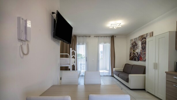 A modern hotel room with a dining area, a sofa, a television, and a painting on the wall. - Studio Apartment "Planet Suite 303 Bibione" with Wi-Fi (San Michele al Tagliamento)
