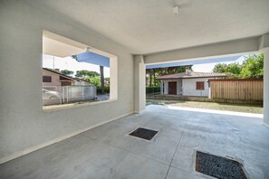 A spacious indoor area with a concrete floor, a window with a metal grill, and a view of a residential neighborhood.