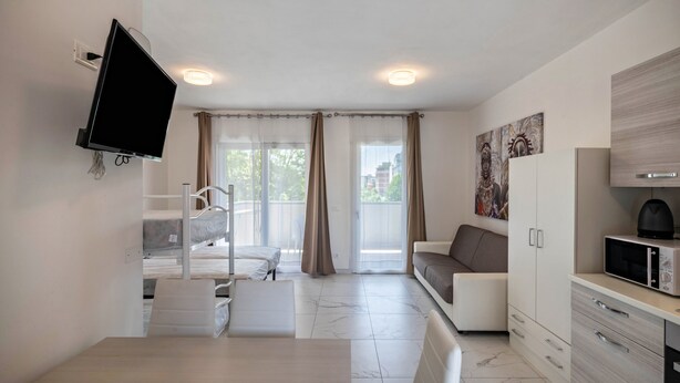 Een moderne hotelkamer met een flatscreen televisie, een eettafel, een bank, een keukenhoek en een balkon met gordijnen.