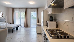 Een moderne keuken met een kookplaat, magnetron en een zithoek met een bank en bed.