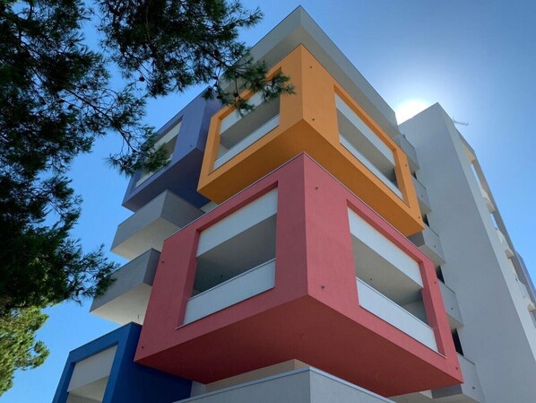 A multi-story building with balconies, clear sky, and trees.