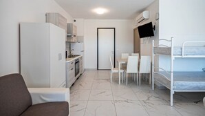 Een compacte kamer met een kitchenette, een eethoek, een stapelbed en een slaapbank.