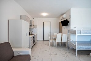 A compact room with a kitchenette, a dining area, a bunk bed, and a sofa.