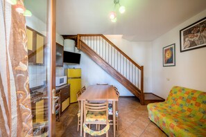 Une cuisine avec une table et des chaises en bois, un escalier, un canapé et un téléviseur fixé au mur.