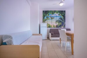 Quarto com cama, escrivaninha, cadeira, refrigerador e parede com mural tropical.