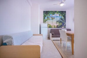 A bedroom with a bed, a small table, a chair, a sofa, and a wall with a tropical mural. - Andromeda B6 Air-Conditioned Apartment (San Michele al Tagliamento)
