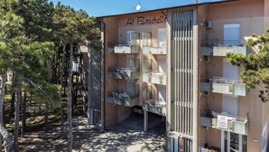 Un immeuble à plusieurs étages doté de balcons, une enseigne indiquant « Al Boschella », et un ciel dégagé.