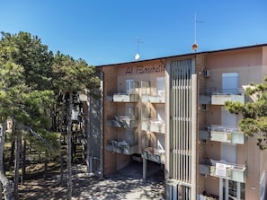 Un immeuble à plusieurs étages doté de balcons, une enseigne indiquant « Al Boschella », et un ciel dégagé.
