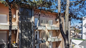 Un immeuble à plusieurs étages doté de balcons, une enseigne indiquant « Al Boschetto », et des arbres au premier plan.