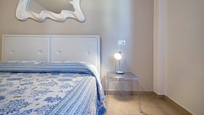 Une chambre à coucher avec un lit, une table de chevet avec une lampe, un miroir et une prise électrique au mur.