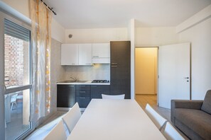 Eine moderne Küche mit weißen Schränken, einem Esstisch und einem grauen Sofa.