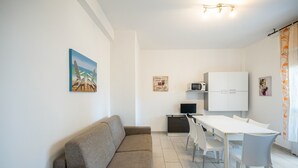 Un salon moderne comprenant un canapé, une table à manger avec des chaises, un coin cuisine avec des placards, un téléviseur et des œuvres d’art accrochées aux murs.