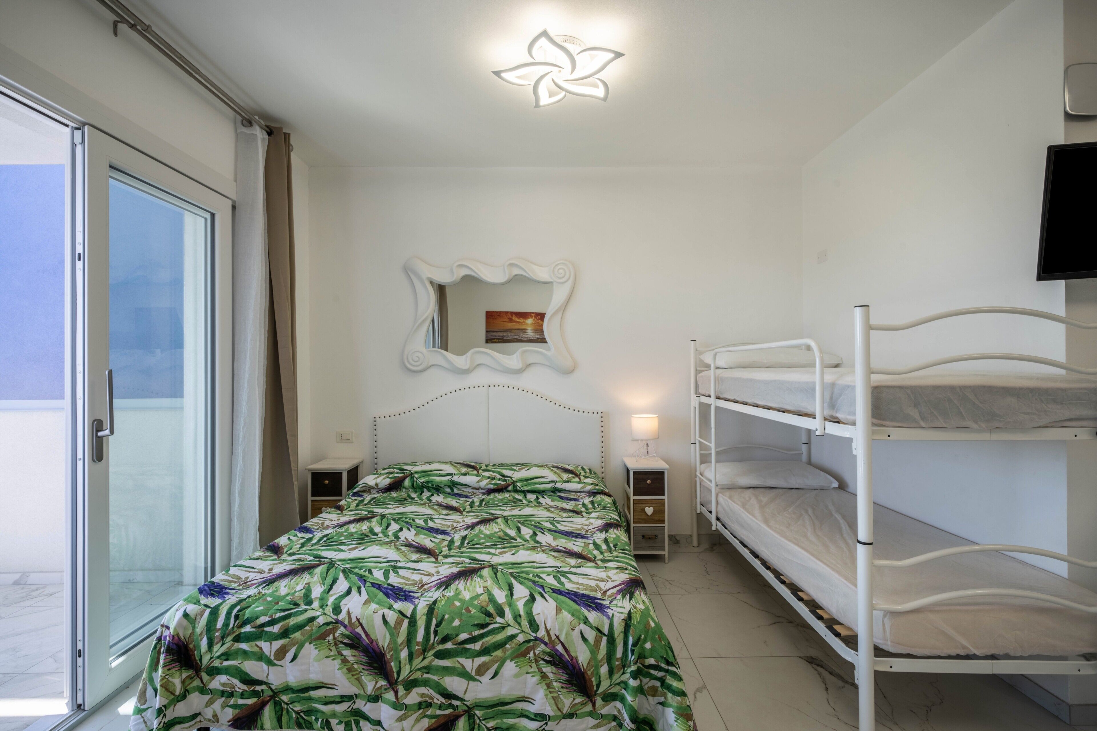 Une chambre à coucher avec un lit, des lits superposés, une table de chevet, un miroir et un téléviseur fixé au mur.