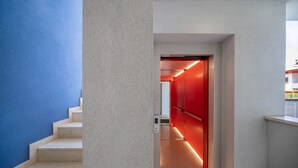 Un ascensor moderno con iluminación roja, pared azul y columna blanca.
