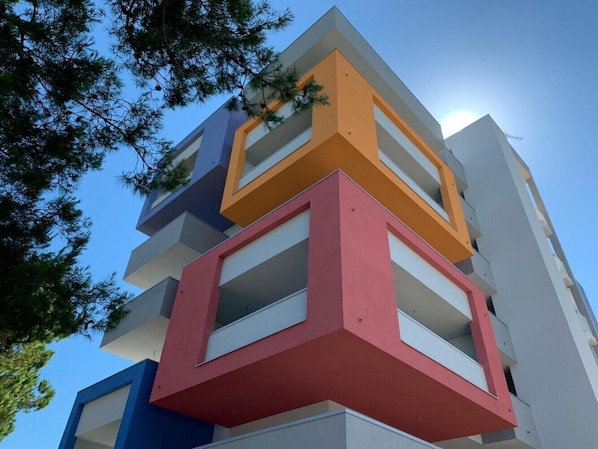 A multi-story building with balconies, clear sky, and trees.