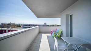 Ein Balkon mit einem weißen Tisch und Stühlen, Blick auf Gebäude und einen klaren Himmel.