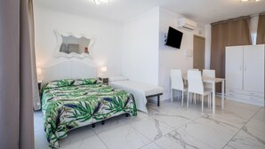 Ein Hotelzimmer mit einem Bett, einem Schreibtisch, Stühlen, einem Fernseher und einer Klimaanlage.