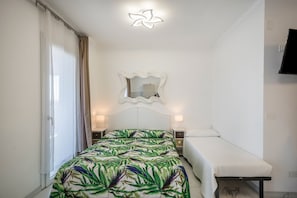 A room with a bed, a bedside table, a small table, a mirror, and a TV mounted on the wall.