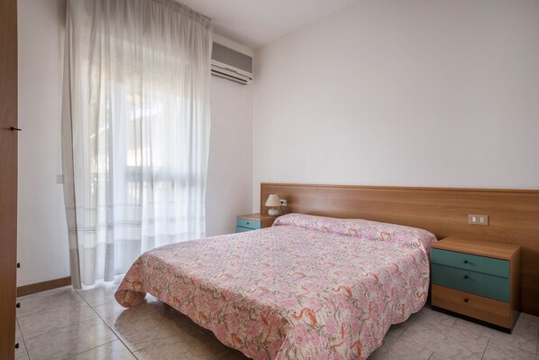 A bedroom with a bed, a nightstand, a drawer, and an air conditioning unit. - Appartamento della Bilancia 4 (Bibione)