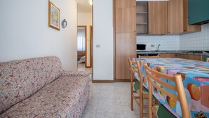Una sala de estar con un sofá, una mesa de comedor con sillas, armarios de madera y una zona de cocina con microondas.