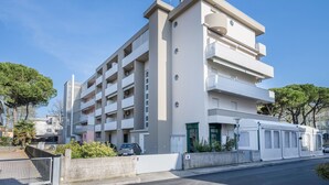 Un edificio residencial de varios pisos con balcones, un acceso con portón y un cielo despejado.