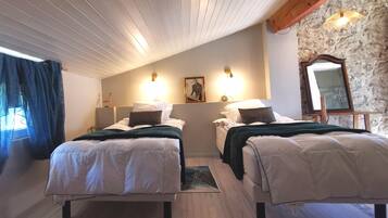 A bedroom with two beds, a wooden ceiling, a stone wall, and a mirror.