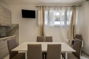 Una cocina moderna con una televisión de pantalla plana, una mesa de comedor con sillas y una ventana con cortinas.