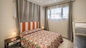 A bedroom with a bed, a bedside table with a lamp, a window with curtains, and a bunk bed. - Appartamento Andromeda 13 (Bibione)