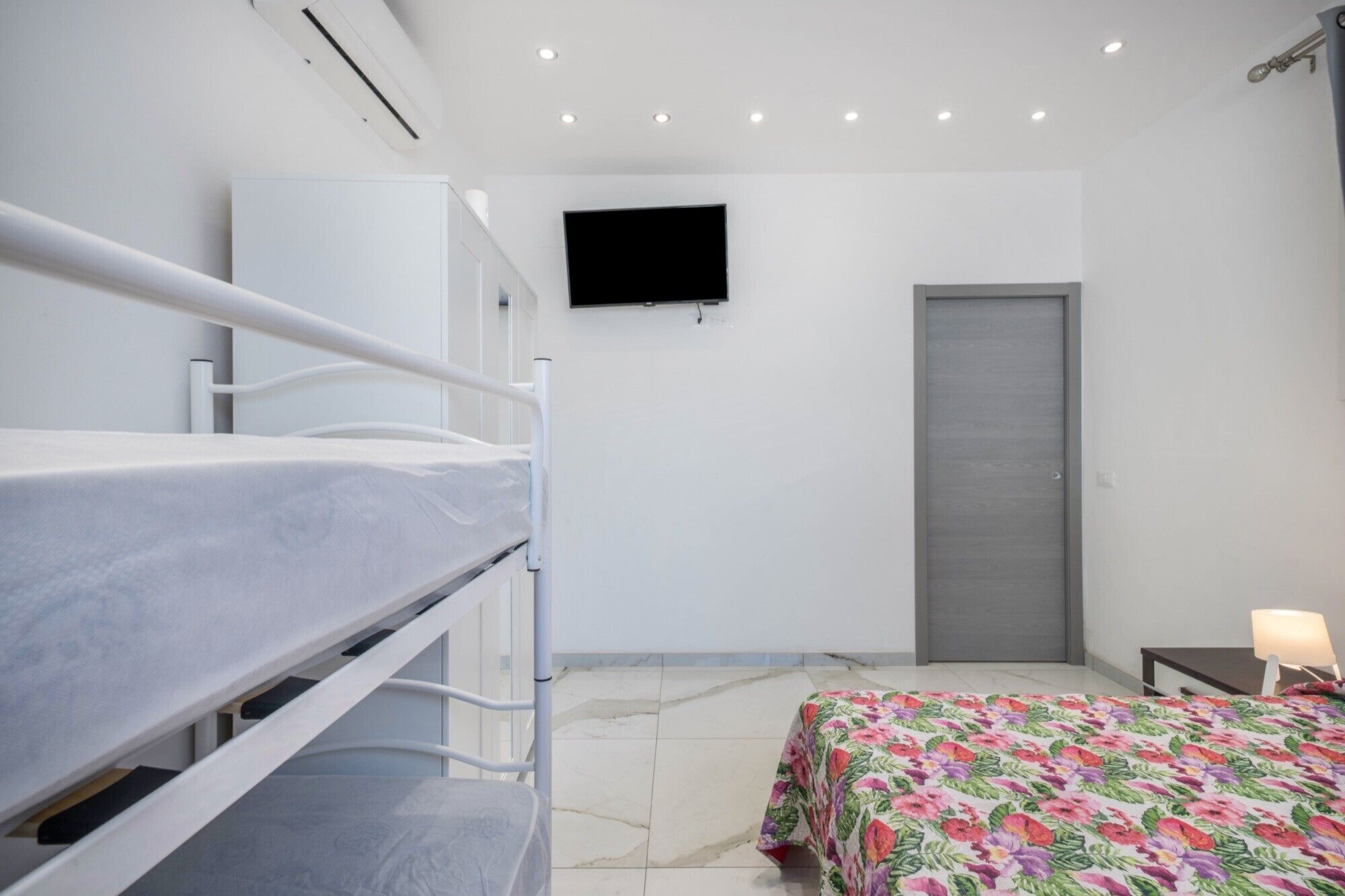 A bedroom with bunk beds, a flat-screen TV, a door, and a bed with a floral bedspread.