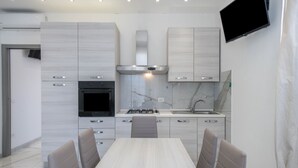 A modern kitchen with a dining table and chairs, built-in oven, stove, and a TV mounted on the wall. - Appartamento Andromeda 13 (Bibione)
